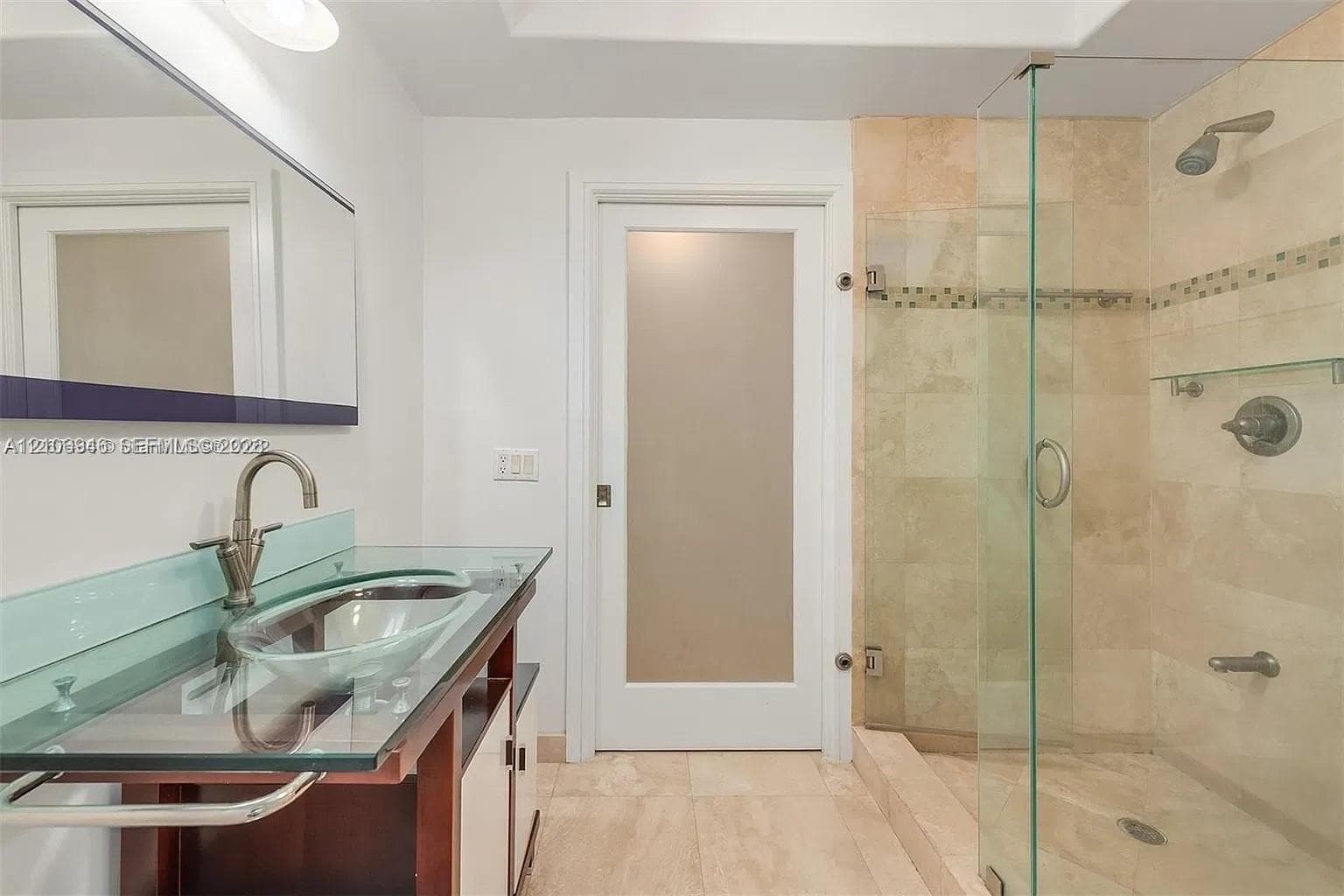 Bathroom featuring a glass-topped vanity with an integrated basin, frosted glass panel door, and a walk-in shower with stone tile surround and frameless glass enclosure