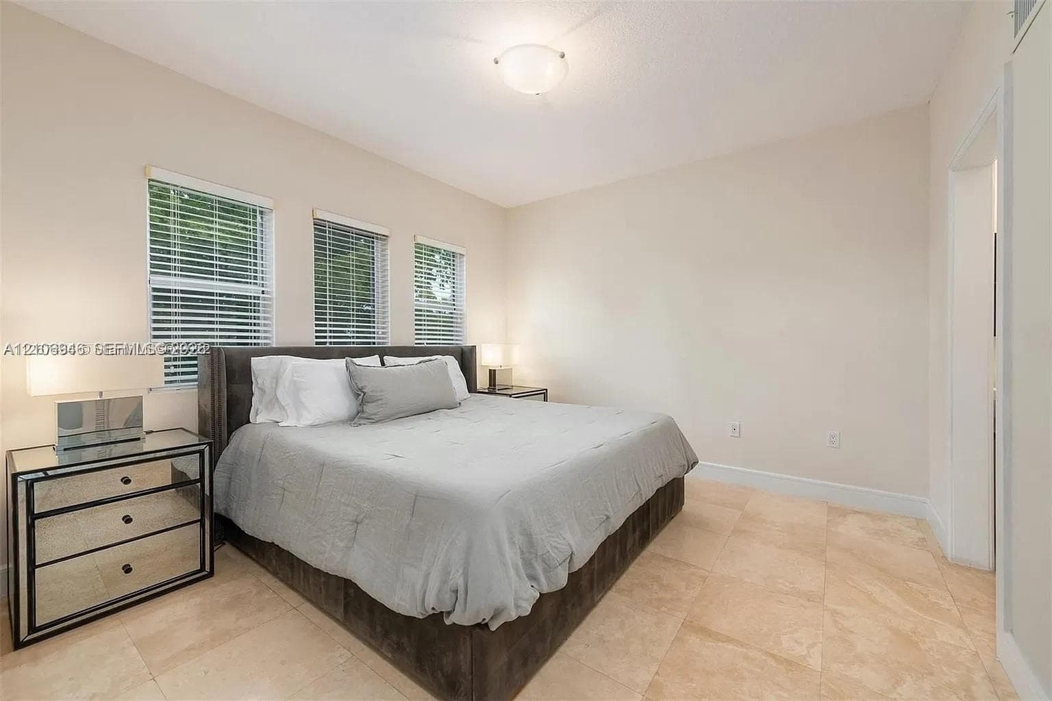 Neutral-toned room featuring large-format tile flooring, three windows with horizontal blinds, and a semi-flush mount ceiling fixture