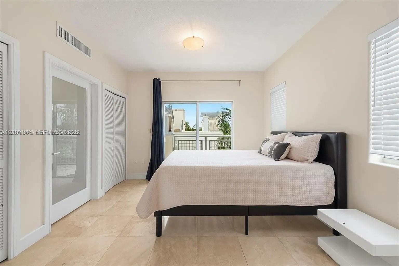 Neutral-toned room featuring large-format tile flooring, sliding glass balcony door, double-panel closet with louvred doors, and single-panel glass-inset entry door