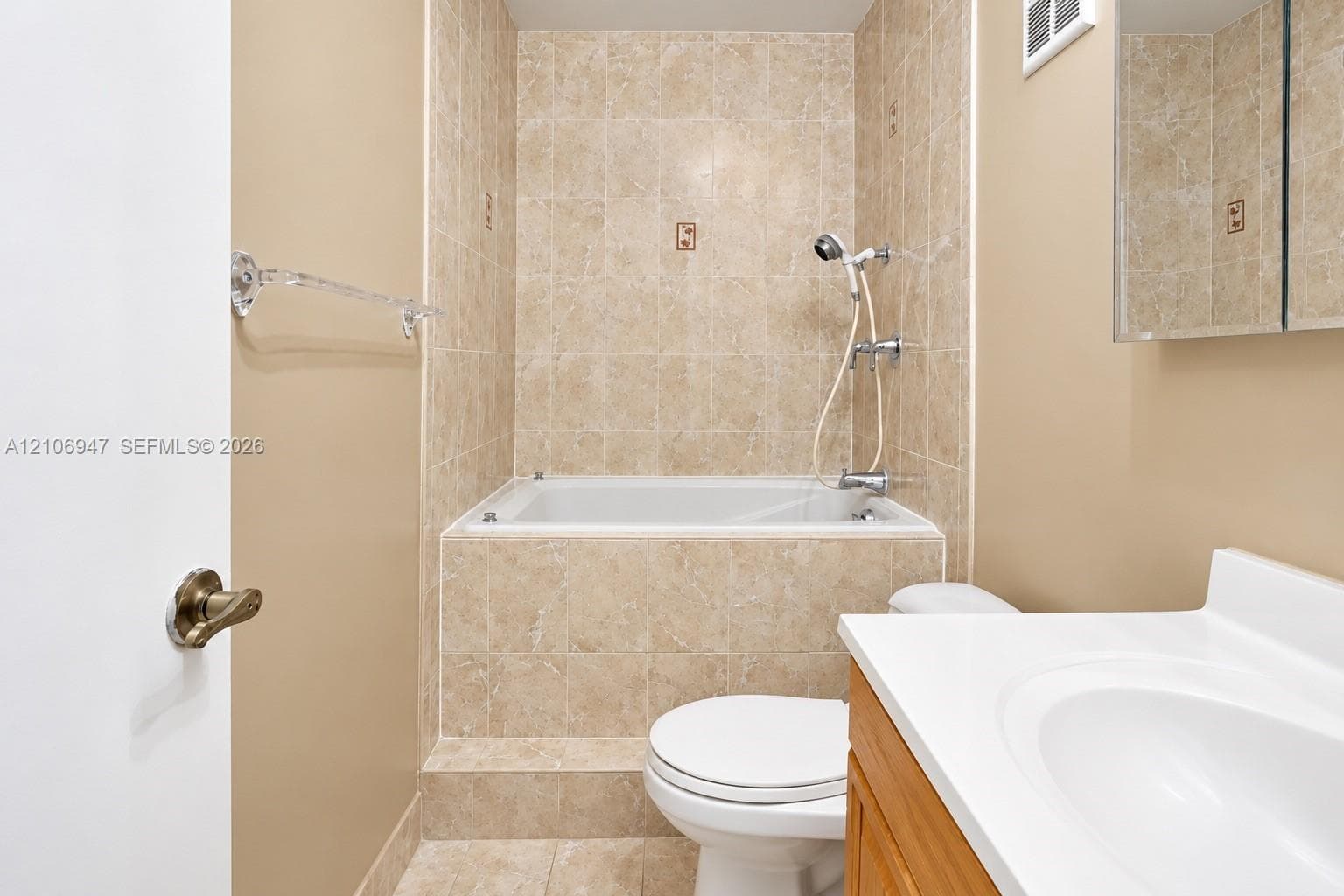 Bathroom featuring a deep-soaking tub with tile surround, wood-finish vanity cabinet, integrated sink, and mirrored medicine cabinet