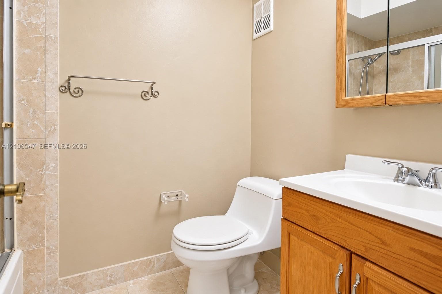 Bathroom featuring a wood-finish vanity with a white countertop, integrated sink, and dual-door medicine cabinet, complemented by tile flooring and tiled shower surrounds