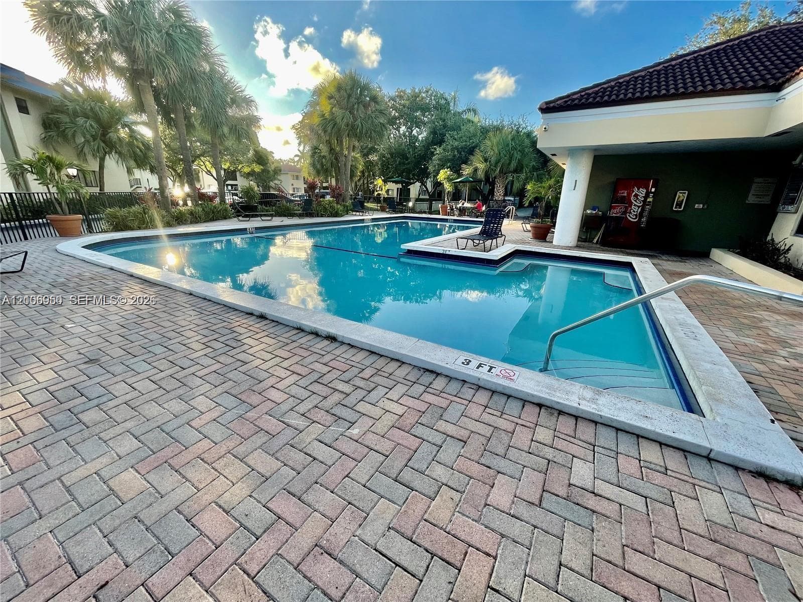 Inground swimming pool with a shallow entry area, surrounded by herringbone-patterned paver decking