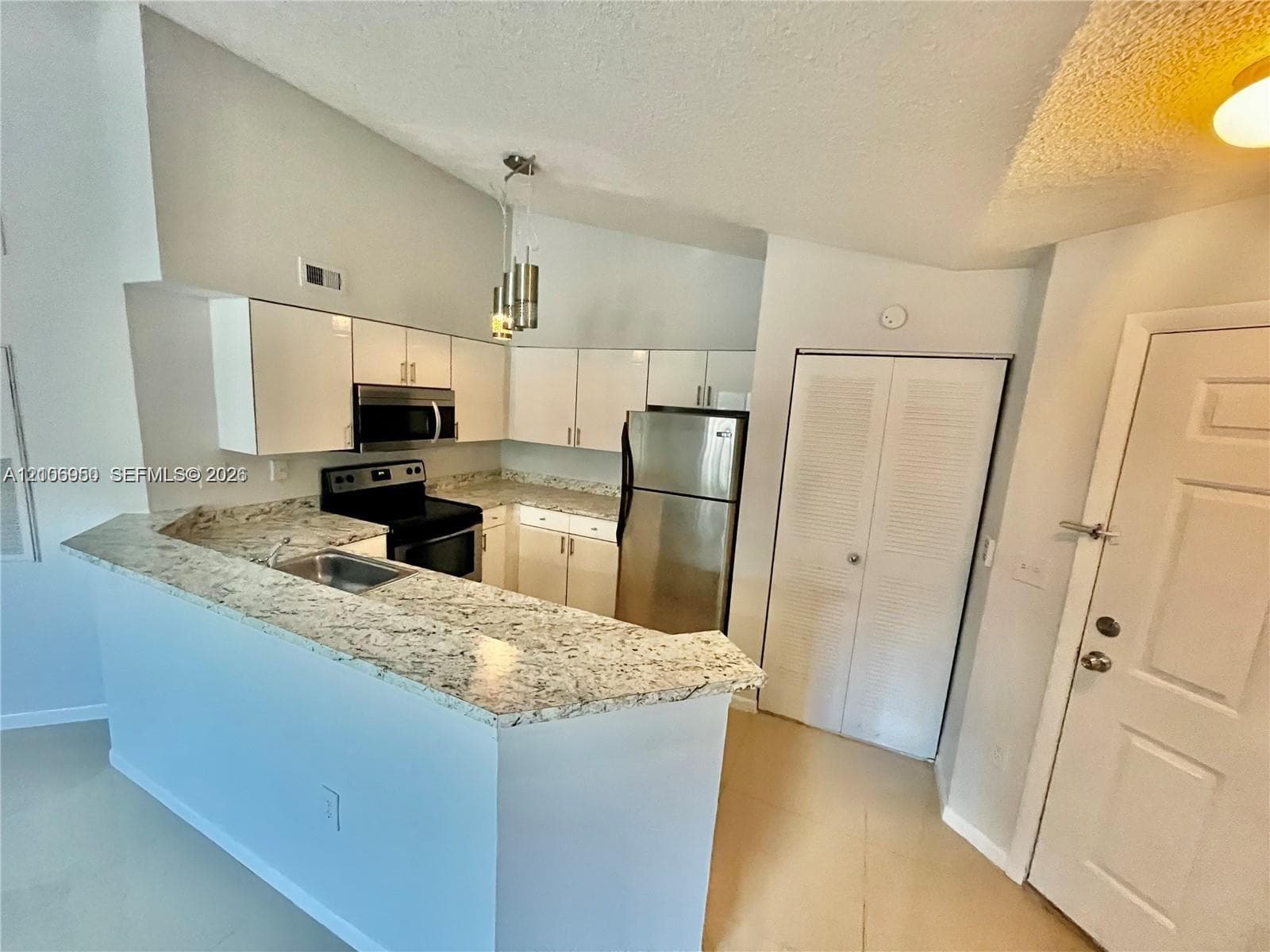 Kitchen featuring stone-finish countertops, stainless steel appliances, flat-panel cabinetry, a stainless steel sink, and a multi-light pendant fixture