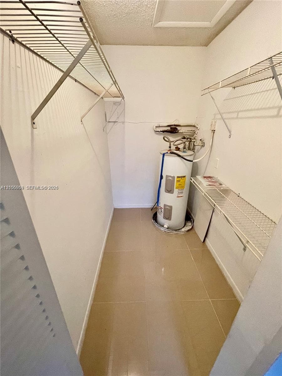 Utility closet featuring tile flooring, metal wall-mounted shelving, and an electric water heater