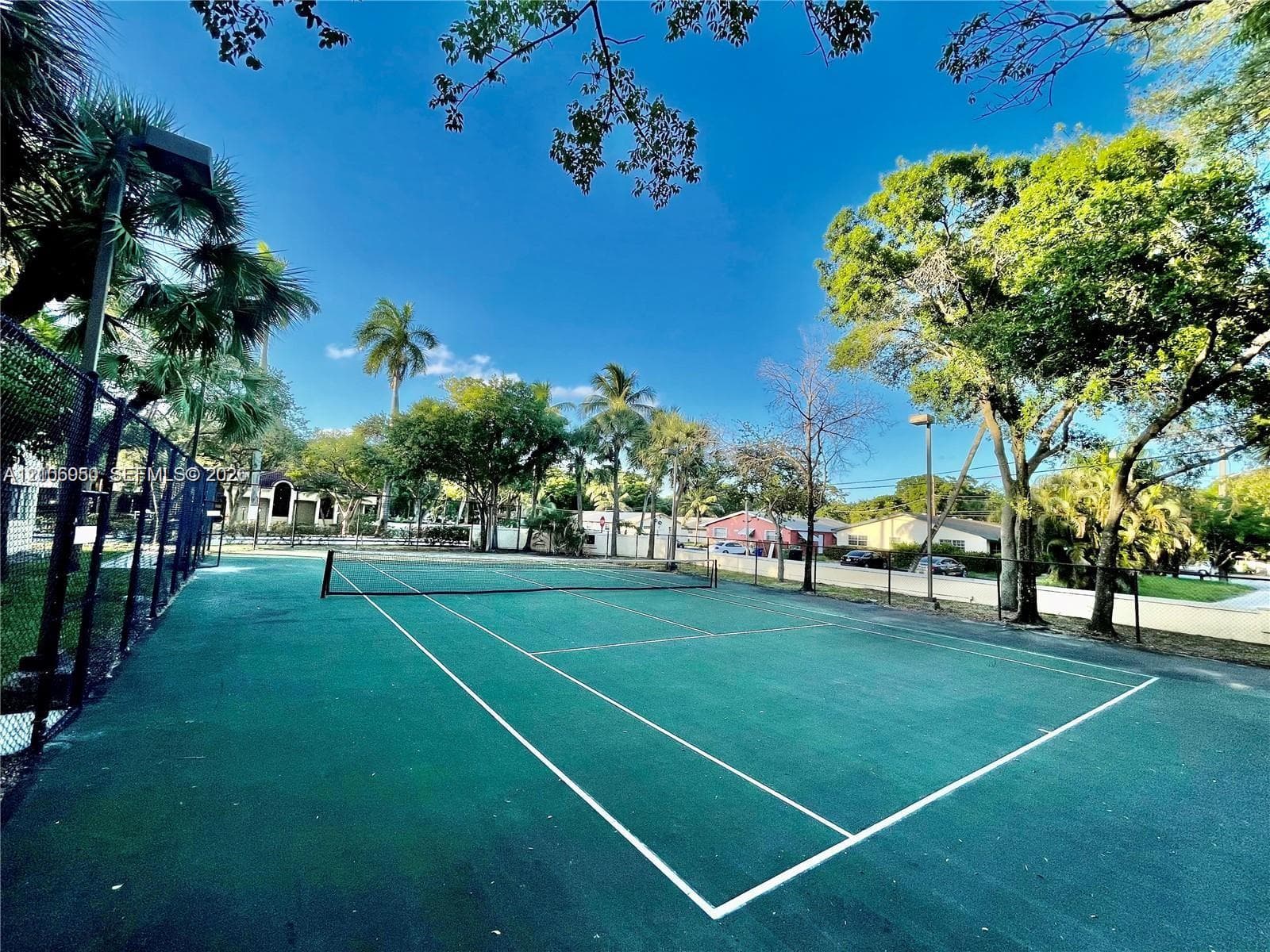 Tennis court with chain-link fencing, painted surface, and surrounding mature trees