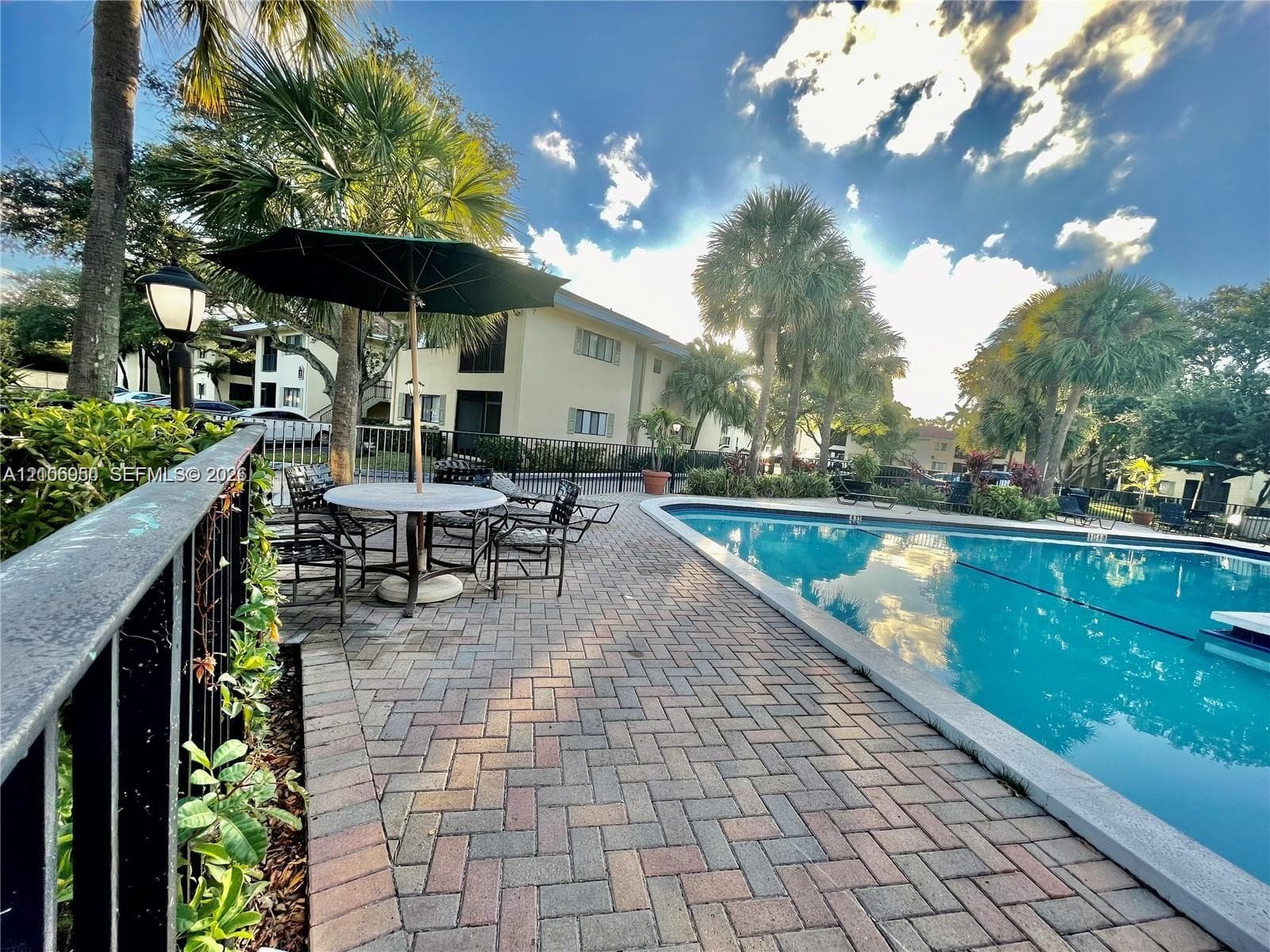 Swimming pool featuring a paved brick deck, metal perimeter fencing, and mature palm trees