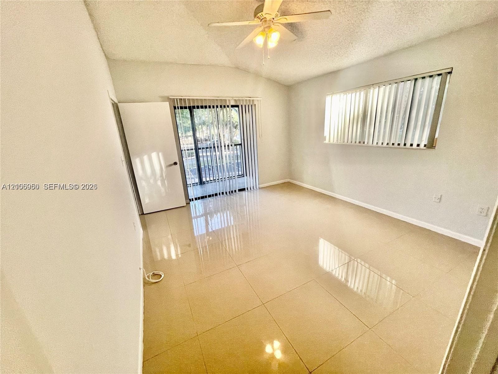 Room featuring neutral large-format tile flooring, vaulted ceilings, a ceiling fan with integrated lighting, and a sliding glass door with vertical blinds