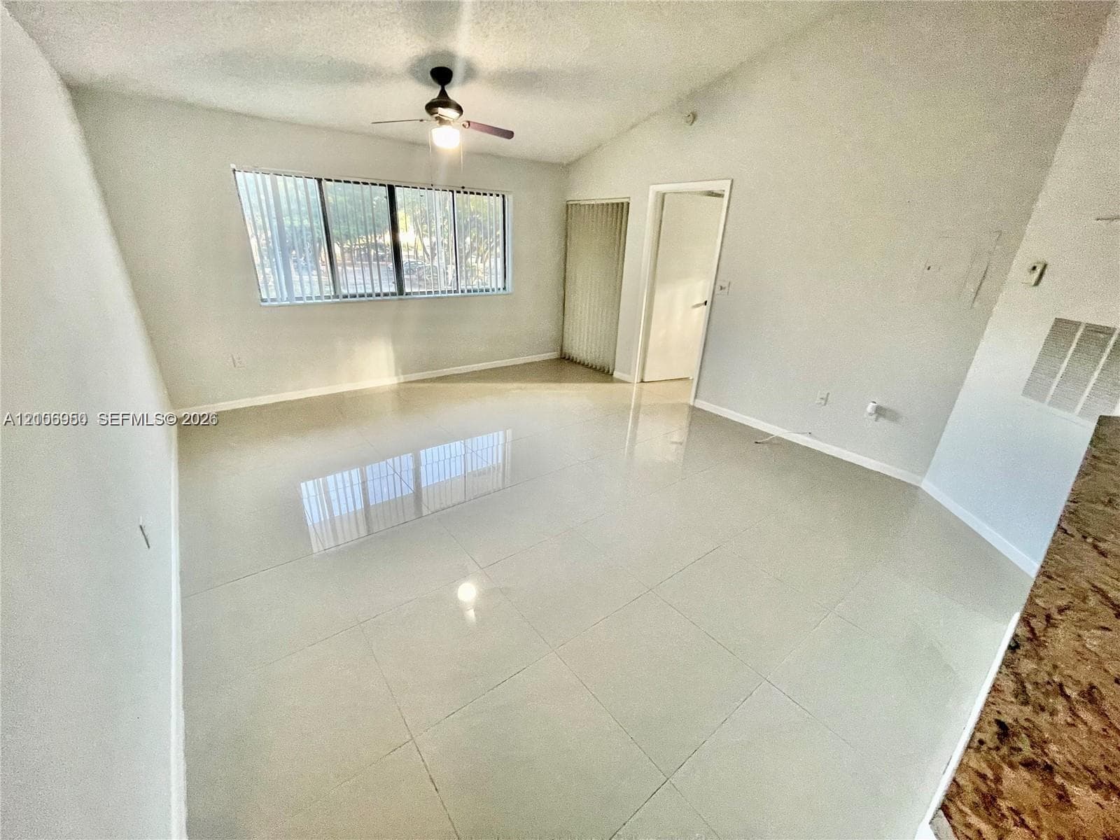 Interior space featuring high ceilings, polished tile flooring, horizontal window blinds, and a ceiling fan with integrated lighting