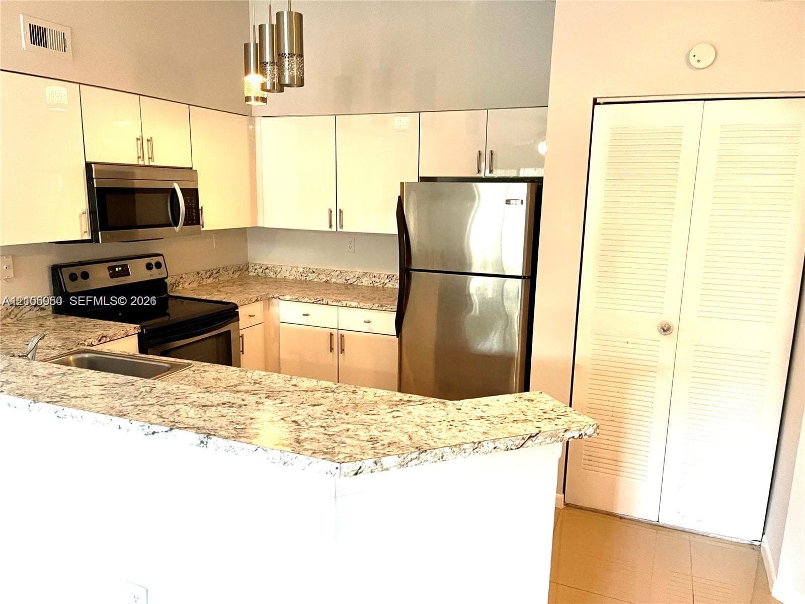 Kitchen featuring flat-panel cabinetry, stone countertops, stainless steel appliances, and pendant lighting
