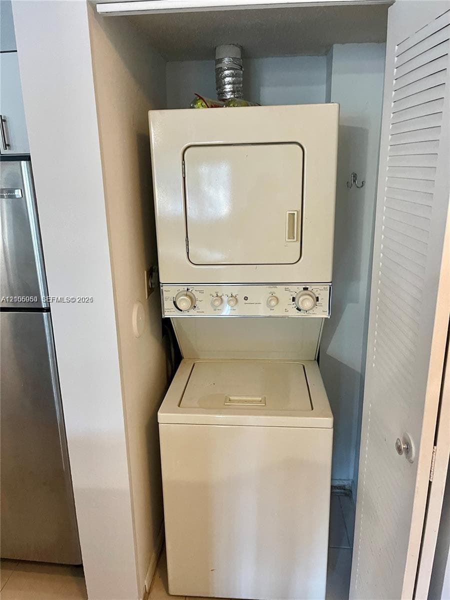 Stacked washer and dryer unit enclosed within a closet featuring a louvered door