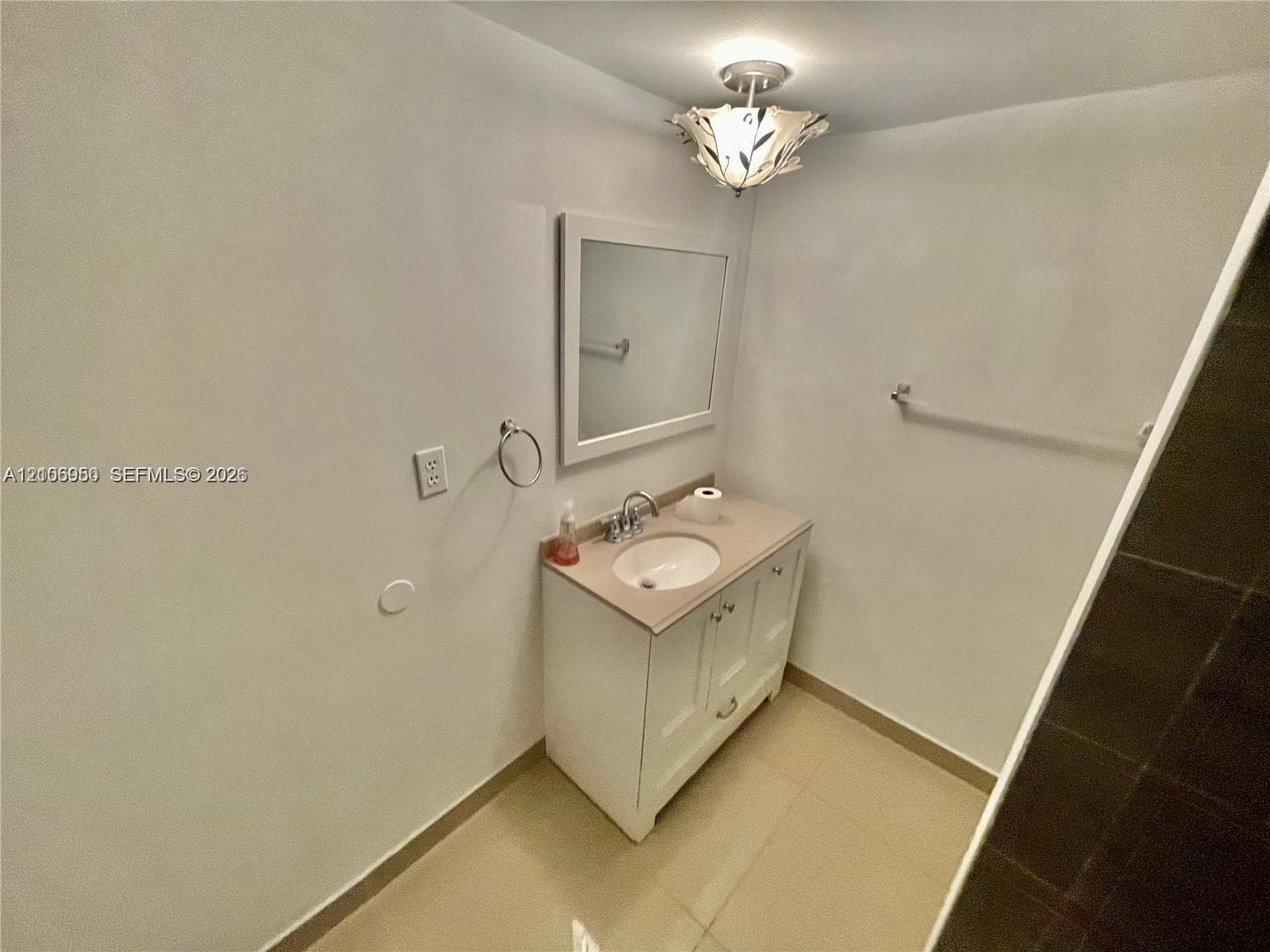 Bathroom featuring a vanity cabinet with an integrated sink, neutral stone-surface countertop, framed wall mirror, decorative overhead light fixture, and tile flooring