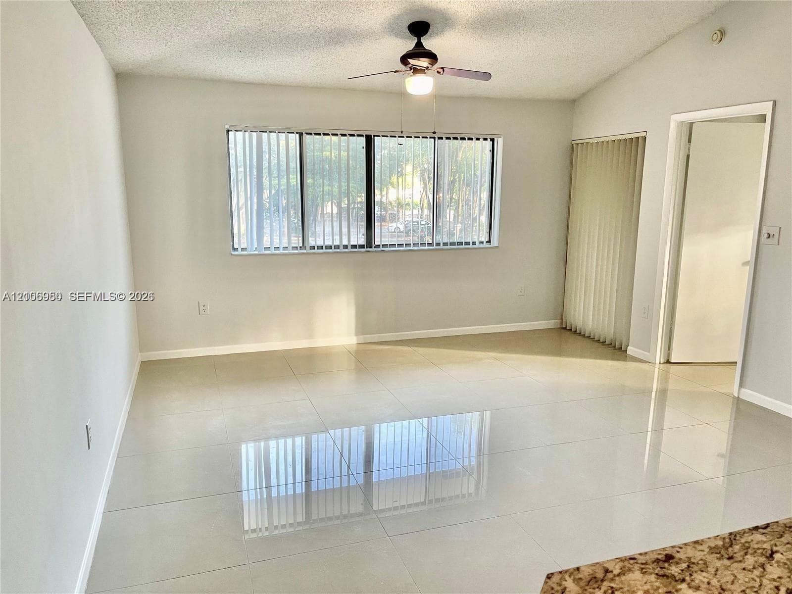 Living space featuring large-format tile flooring, multi-pane window, ceiling fan with integrated light fixture, and vertical window blinds