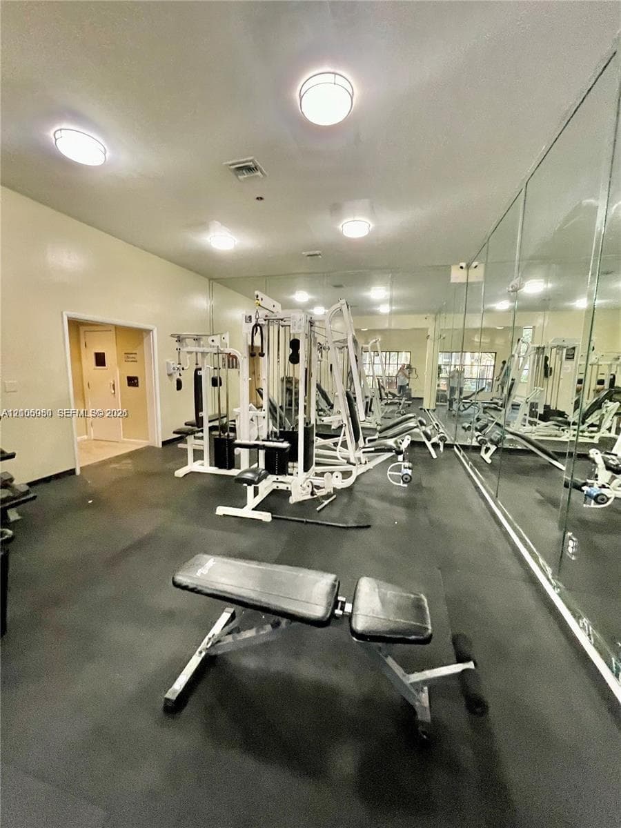 Fitness facility featuring full-wall mirrors, durable rubberized flooring, and recessed ceiling lighting