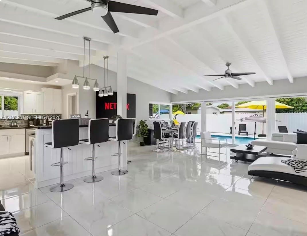 Open-concept interior featuring vaulted, beamed ceilings, oversized tile flooring, a kitchen island with stone countertops, and multiple sliding glass doors