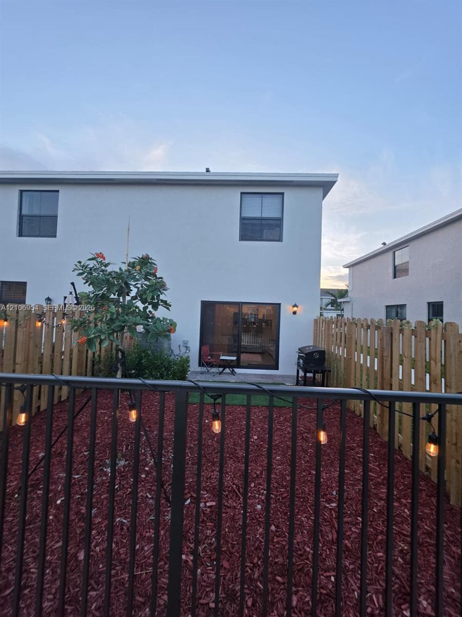 Fenced backyard featuring wood-tone privacy screening, black metal perimeter railing, red-toned mulch ground cover, and sliding glass doors
