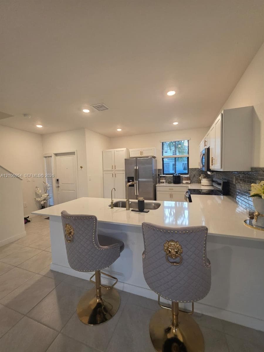 Kitchen featuring white shaker-style cabinetry, solid-surface countertops, recessed lighting, and large-format tile flooring