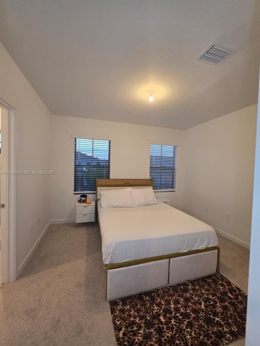 Neutral-toned interior space featuring light-colored wall-to-wall carpeting, two dual-pane windows, and minimalist ceiling-mounted lighting