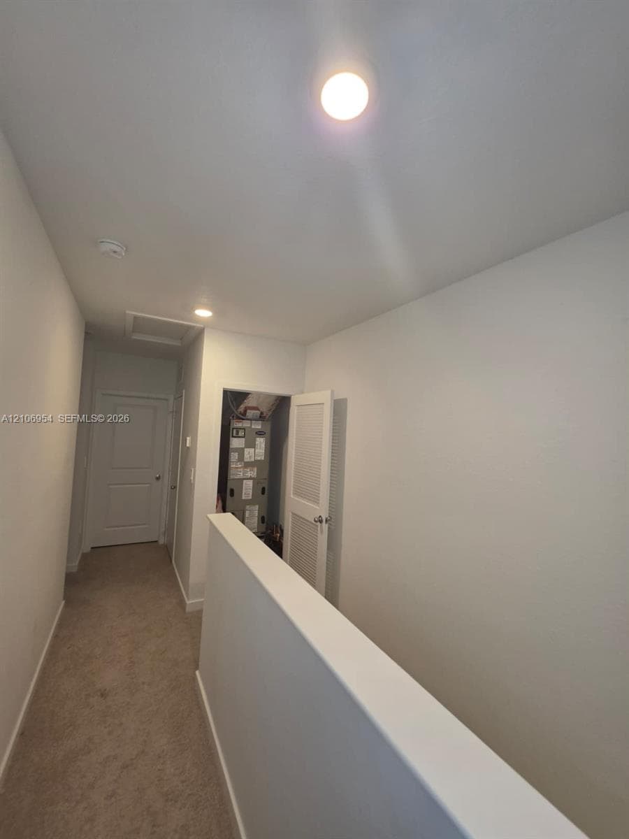 Hallway featuring neutral carpet flooring, recessed ceiling lighting, and louvered door access to utility mechanicals