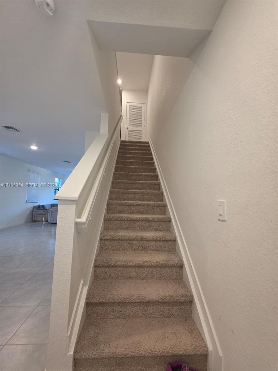 Staircase featuring wall-to-wall carpeting, painted wooden handrails, and louvered door access