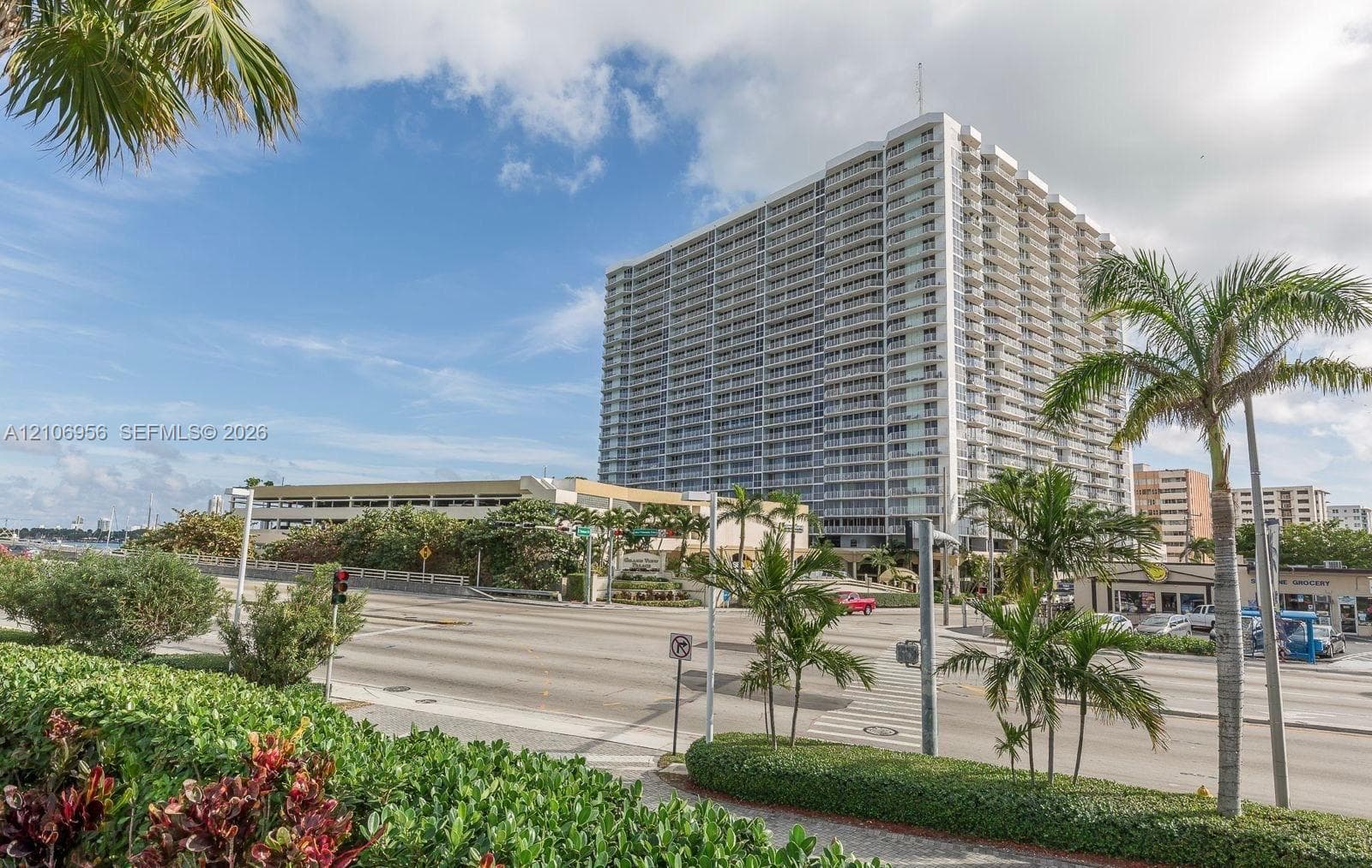 High-rise residential building featuring expansive floor-to-ceiling balcony glass, structured parking facility, and professional landscape design