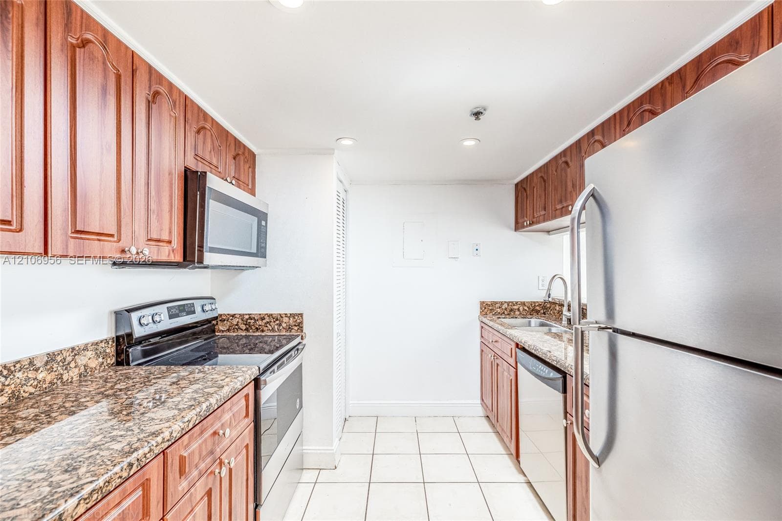 Kitchen featuring wood cabinetry, stone countertops, stainless steel appliances, ceramic tile flooring, and recessed lighting