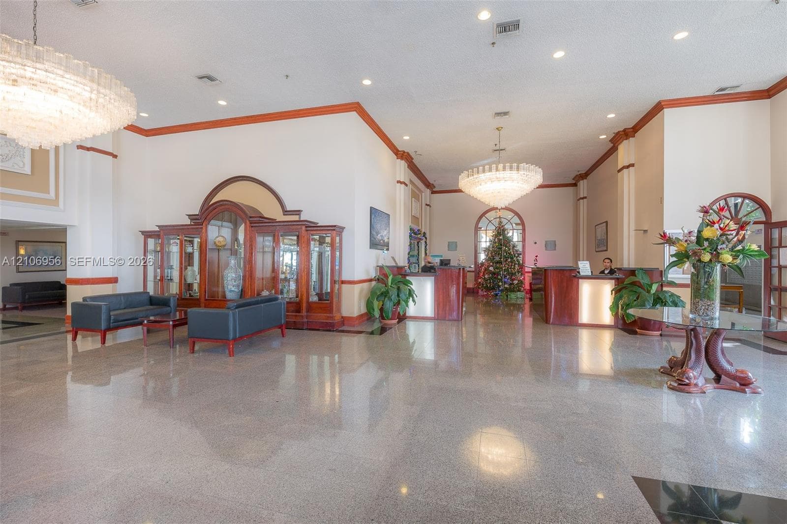 Spacious lobby featuring polished stone flooring, vaulted ceilings, dual tiered crystal chandeliers, wood-trimmed built-in display cabinetry, and recessed lighting