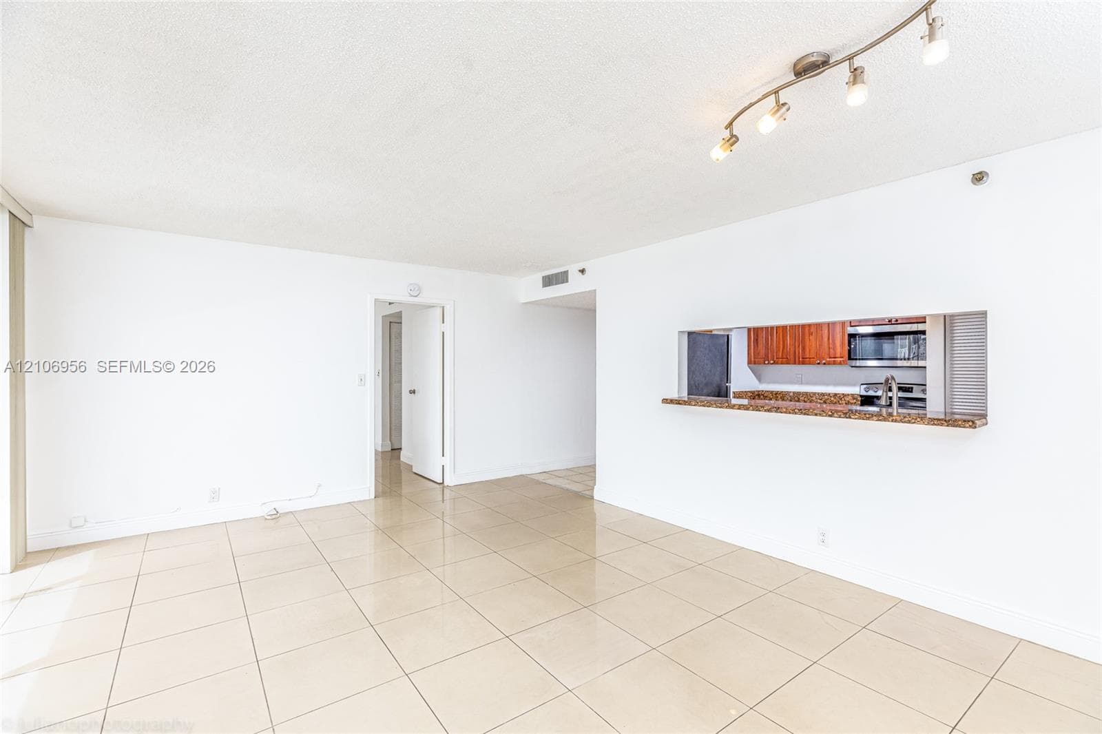 Open-concept living space featuring large-format tile flooring, a pass-through breakfast bar with stone-finish countertop, and adjustable track lighting