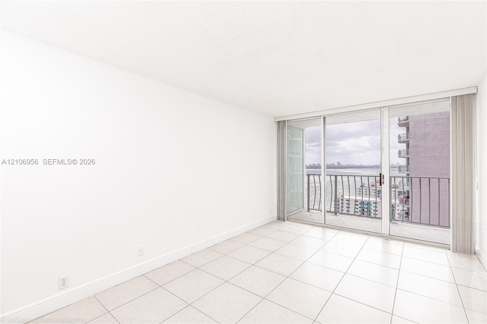 Neutral tile flooring, floor-to-ceiling glass sliding doors, and a private balcony featuring metal railings