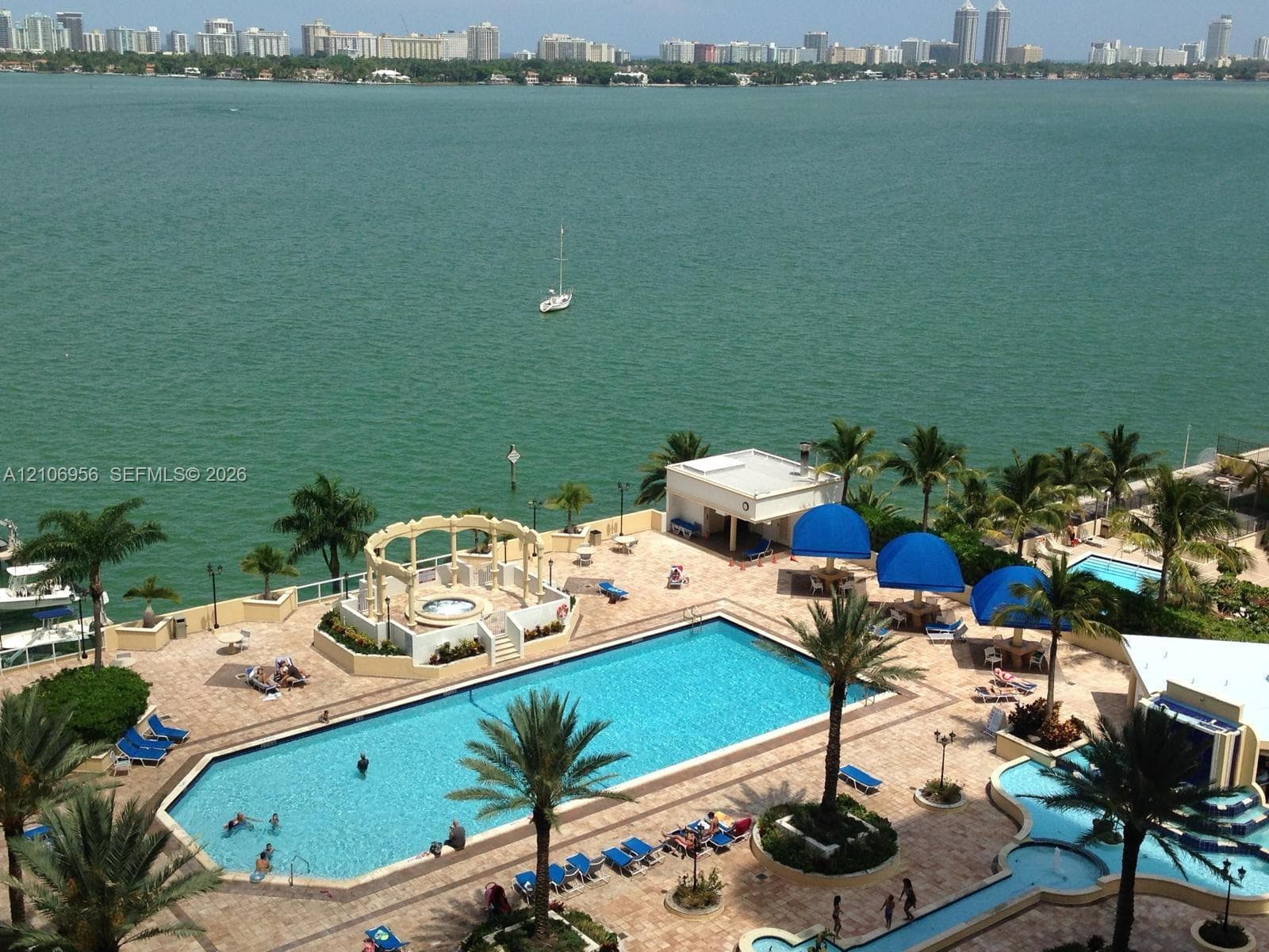 Waterfront pool area featuring stone paver decking, a raised circular spa with a pergola, and palm tree landscaping