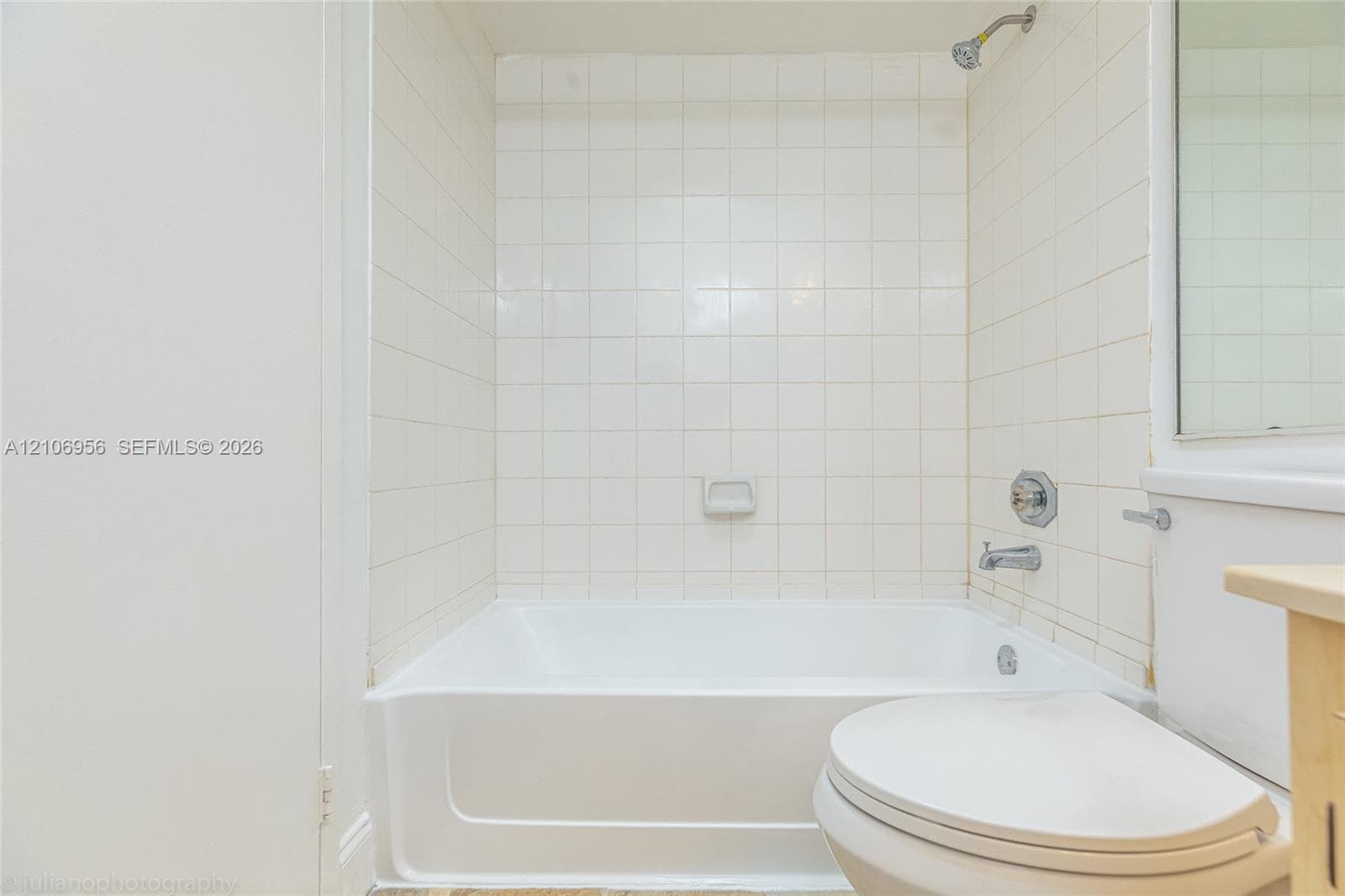 Bathroom featuring a white porcelain tub, square wall tiling, chrome shower fixtures, and a recessed soap dish