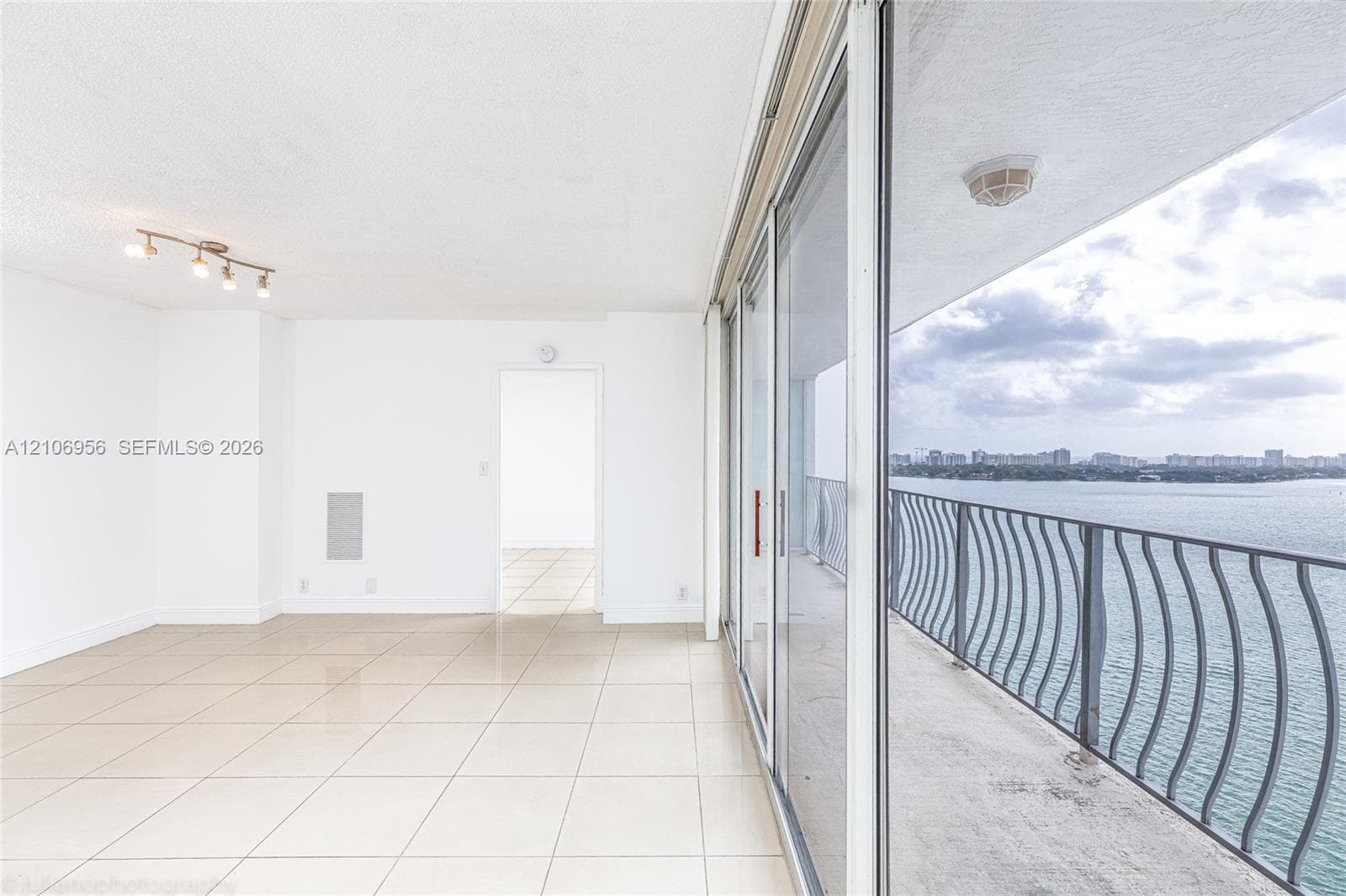 Interior space featuring oversized floor tiles, sliding glass balcony doors, a multi-bulb track lighting fixture, and a metal balcony railing