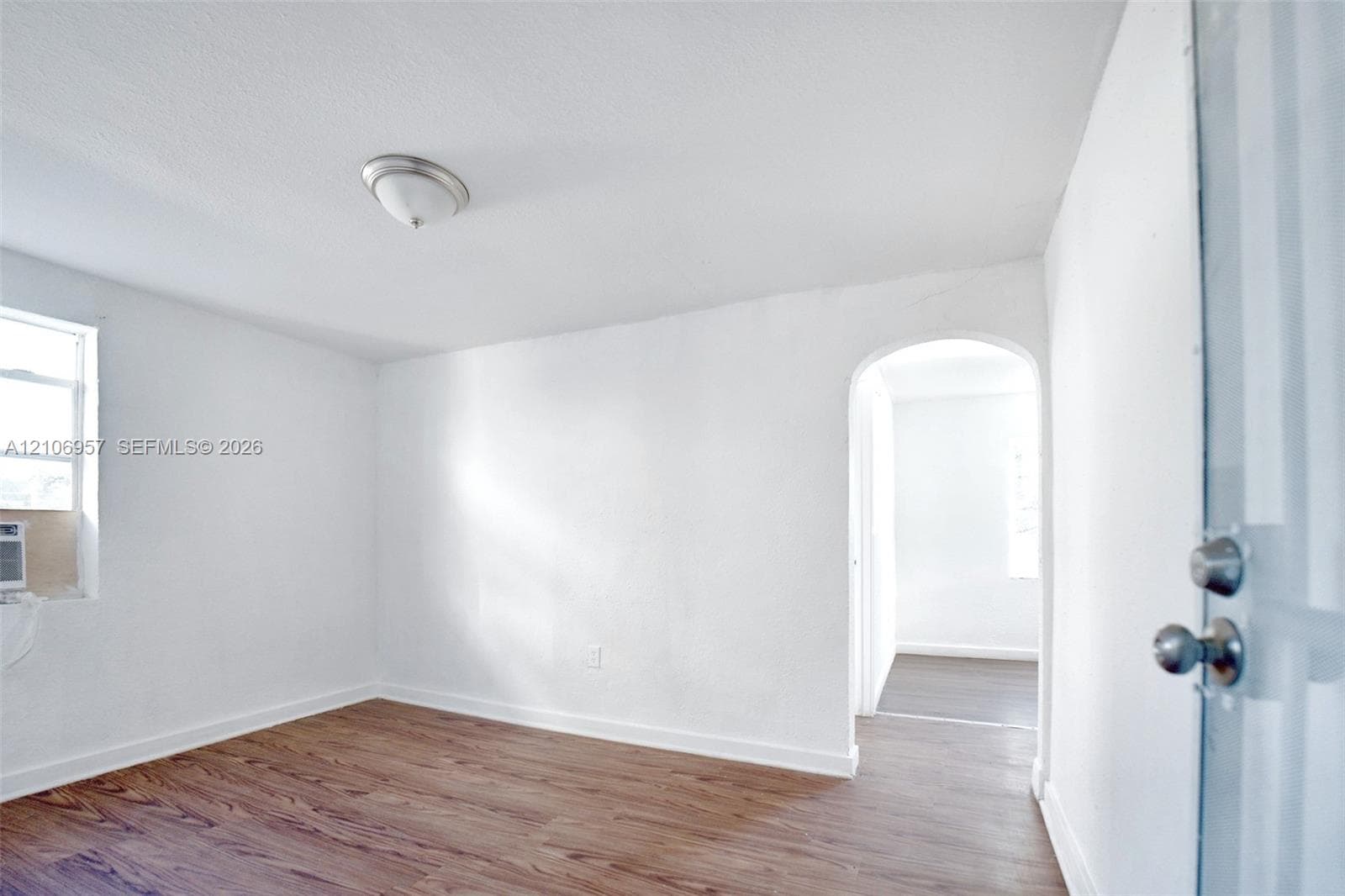 Room featuring wood-finish flooring, white walls, an arched entryway, and a flush-mount ceiling light fixture