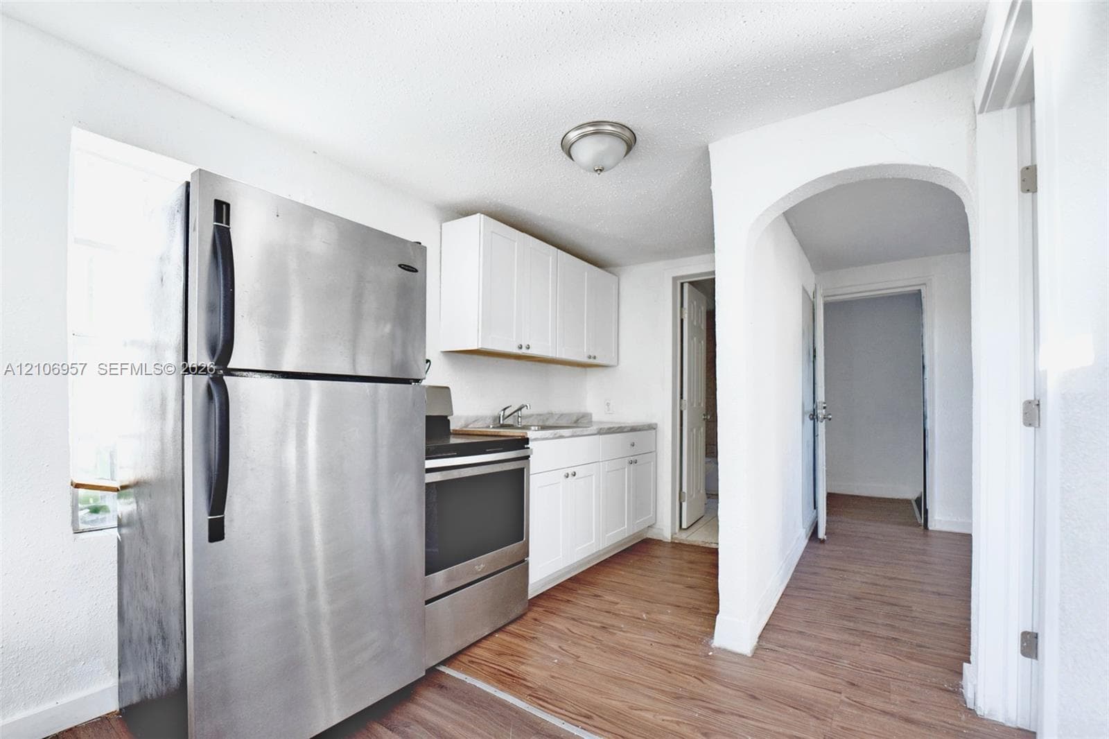 Kitchen featuring stainless steel refrigerator and range, white cabinetry, solid-surface countertops, and wood-finish flooring
