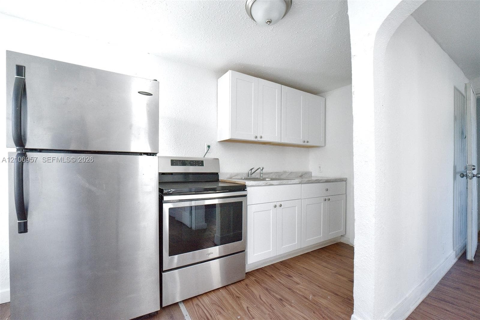 Kitchen featuring white cabinetry, wood-finish flooring, stainless steel refrigerator, stainless steel electric range, and stone-finish countertop