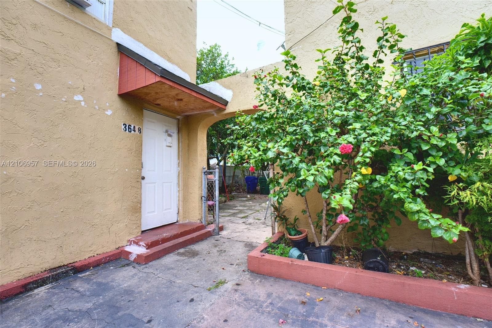 Stucco exterior featuring a covered entryway, paved concrete patio area, and a raised masonry planter