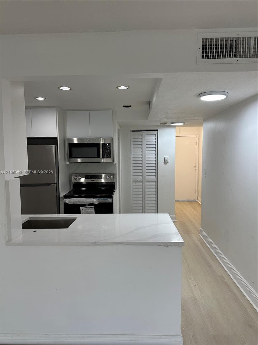 Kitchen featuring white cabinetry, stone-finish countertops, stainless steel appliances, recessed lighting, and wood-finish flooring
