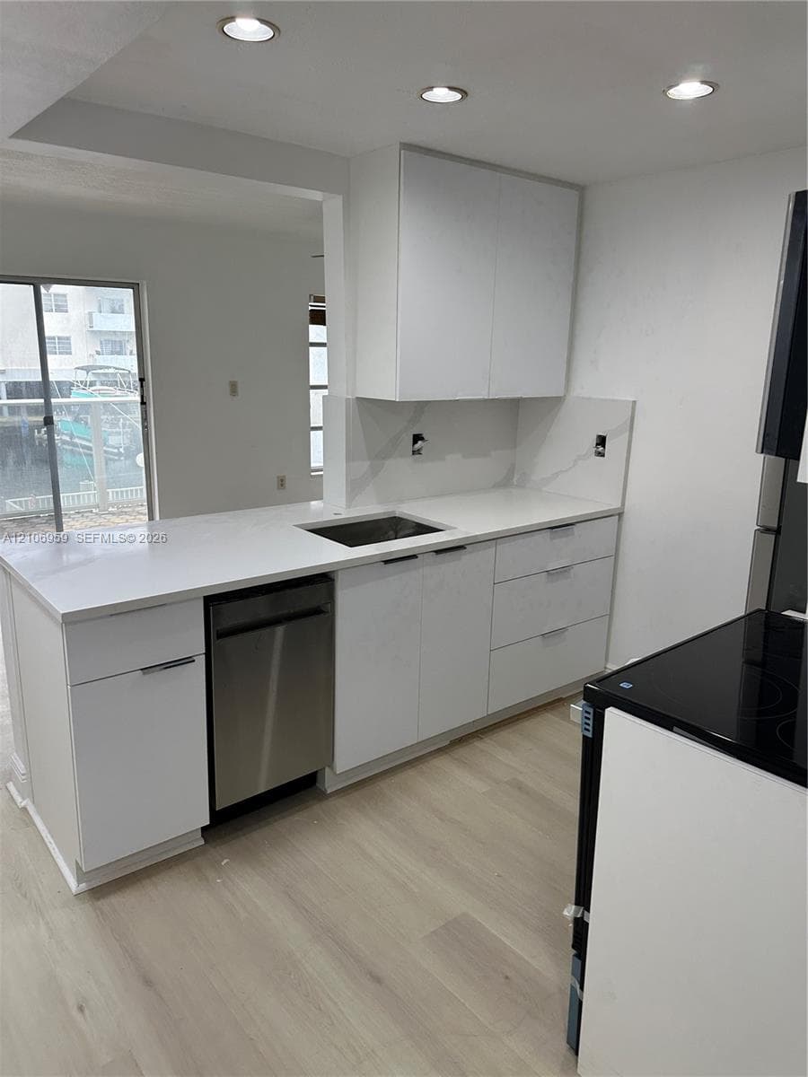 Kitchen featuring white flat-panel cabinetry, light-toned stone-finish countertops, stainless steel dishwasher, integrated sink, and wood-finish flooring