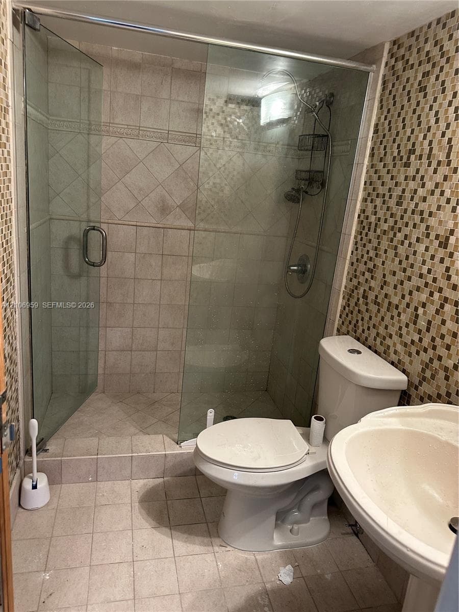 Glass-enclosed shower with a rainfall showerhead, ceramic tile surround, pedestal sink, and mosaic tile accent wall
