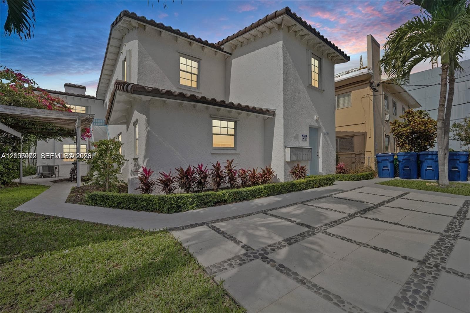 Stucco exterior featuring tile roof accents, multi-pane windows, and a paved stone driveway with pebble inlays