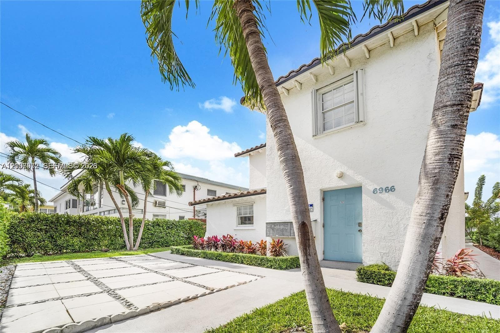 Stucco exterior featuring a tile roof, paved grid driveway, and mature palm trees