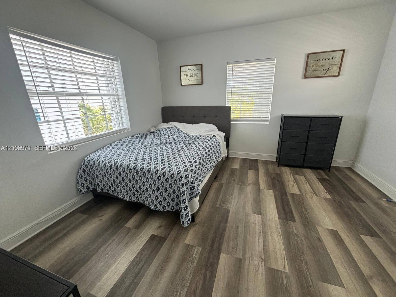 Room featuring wood-finish flooring, dual windows with horizontal blinds, and neutral wall tones