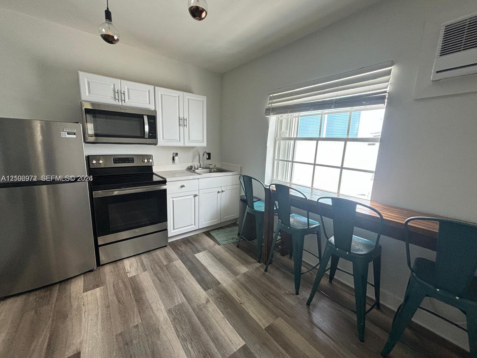 Kitchen featuring white cabinetry, stainless steel appliances, wood-finish flooring, a built-in wood-top counter, and pendant lighting