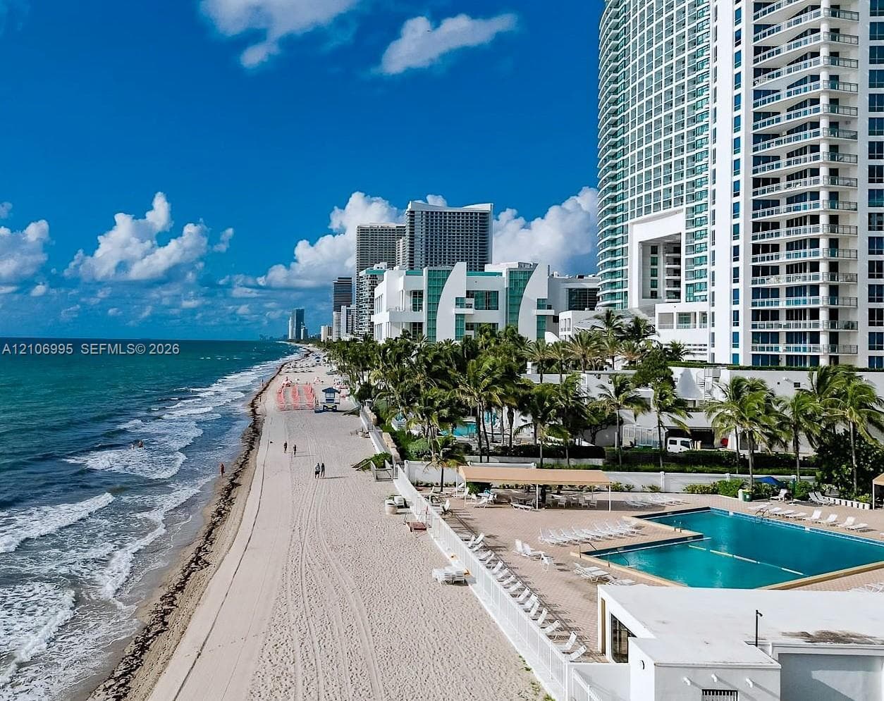 Oceanfront high-rise building featuring a multi-level swimming pool, expansive pool deck, and direct sandy beach access