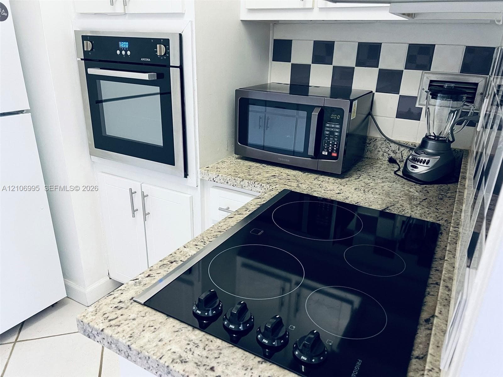 Kitchen featuring stone countertops, white cabinetry, a built-in wall oven, a glass-top electric cooktop, and a checkerboard-pattern backsplash