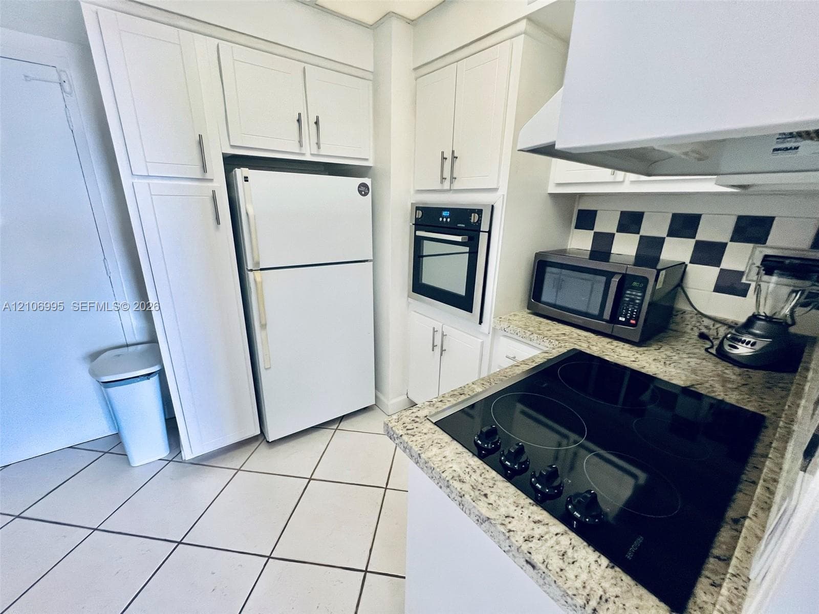 Kitchen featuring white cabinetry, stone-finish countertops, checkerboard backsplash, built-in oven, and a ceramic cooktop