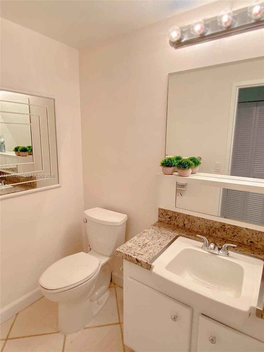 Bathroom featuring a vanity with a stone-finish countertop, undermount sink, multi-bulb overhead lighting, oversized wall mirror, and neutral tile flooring