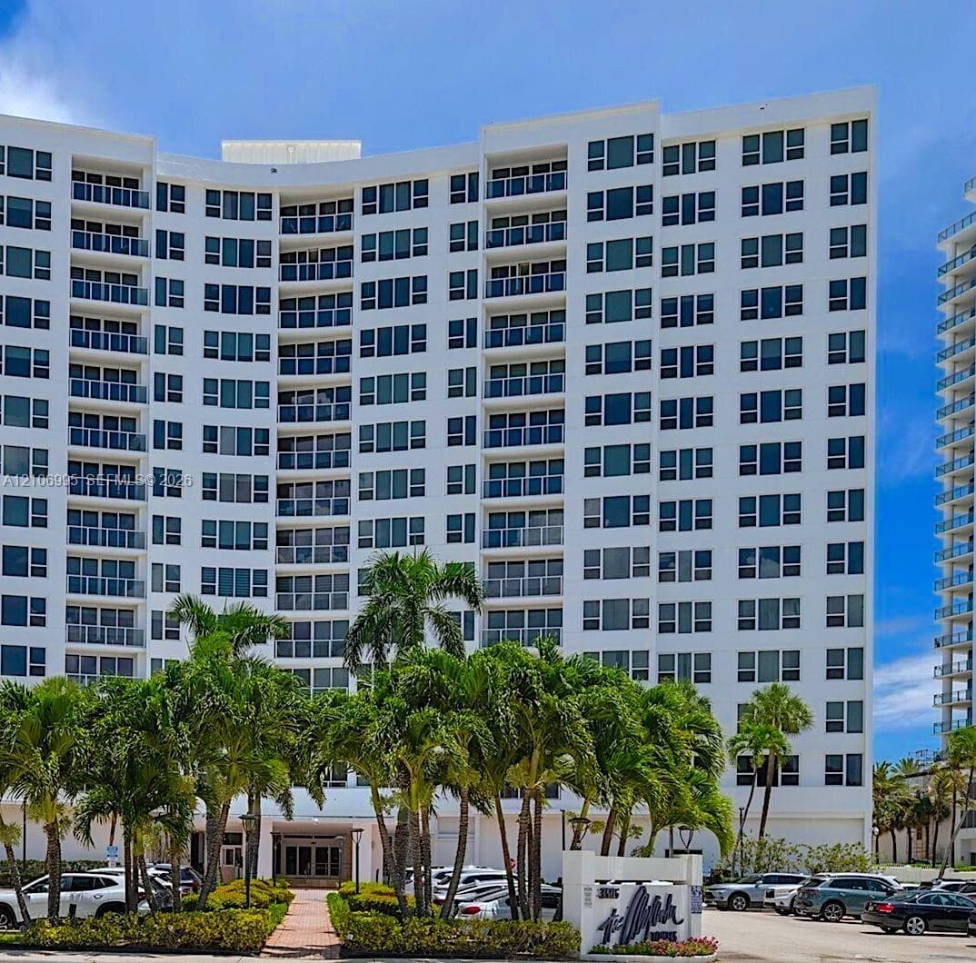 High-rise building exterior featuring a curved facade, uniform glass-paneled balconies, and mature palm tree landscaping