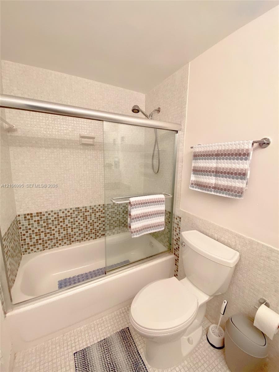 Bathroom featuring a shower-tub combination with sliding glass doors, multi-toned mosaic tile accents, and a wall-mounted hand-held shower head