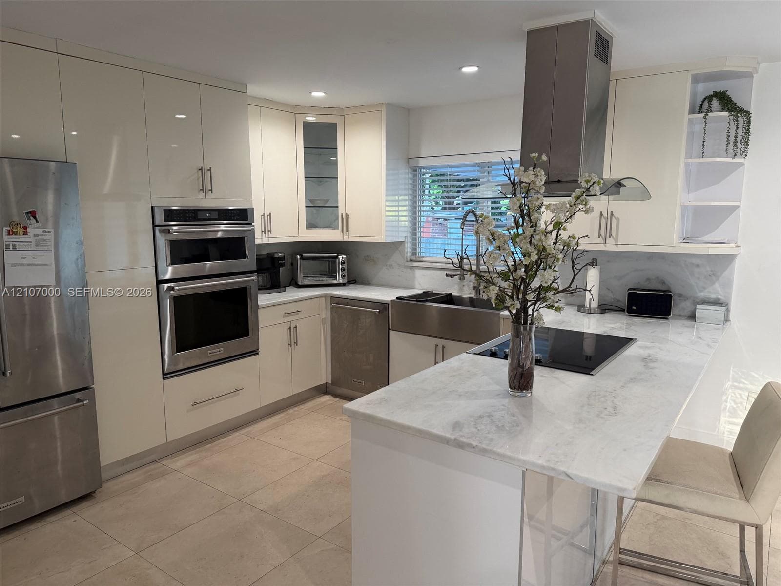 Kitchen featuring high-gloss cabinetry, stone-surface countertops, a stainless steel farmhouse sink, built-in double wall ovens, and an integrated stainless steel range hood