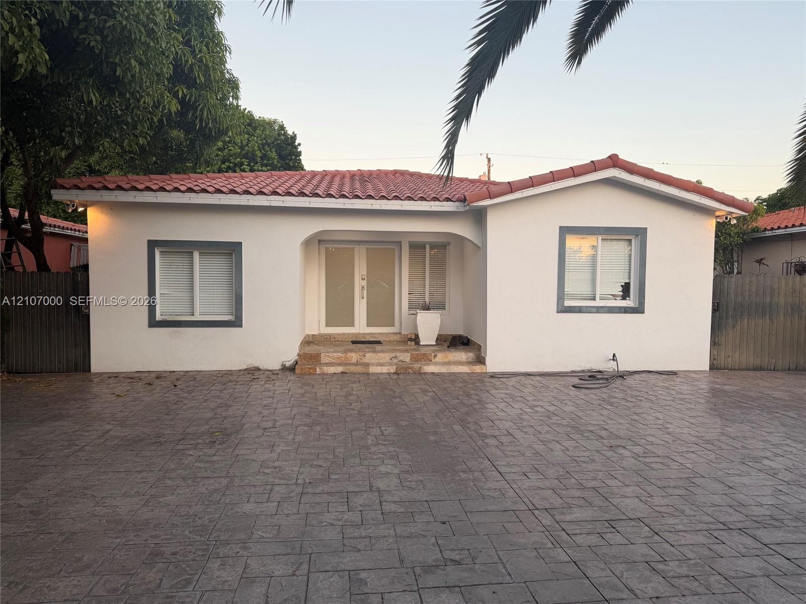 Stucco exterior featuring a terracotta tile roof, stone-finish entryway steps, and double-entry glass paneled doors